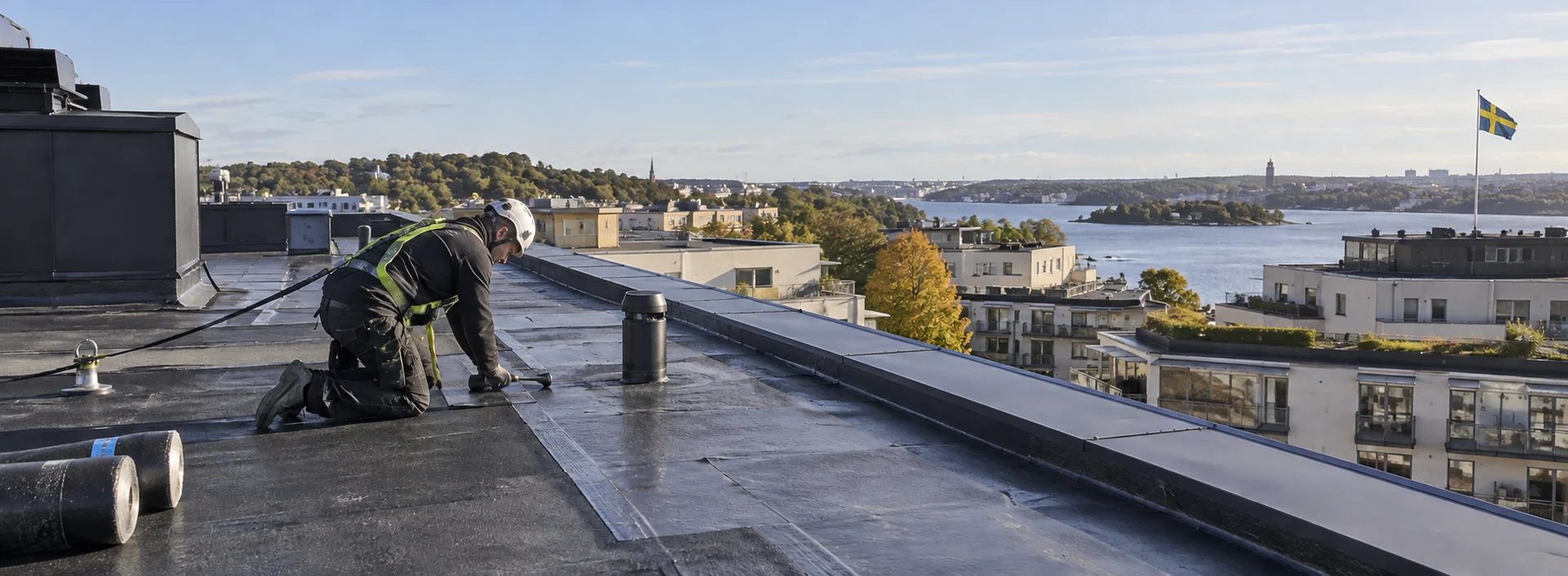 Takläggare med hjälm och säkerhetssele på ett platt tak med stadspanorama