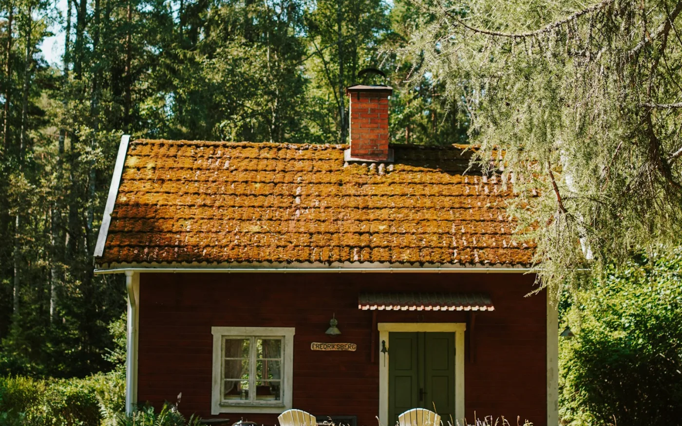 Mossbevuxet tegeltak och hängränna på ett rött trähus i Sverige