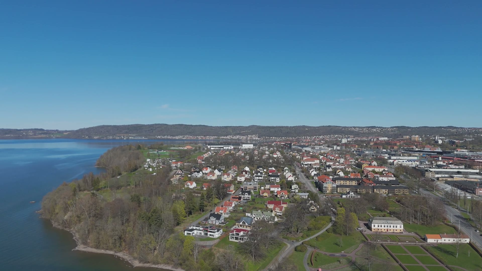 Flygvy över svenska småhus, trädgårdar och tak vid en sjö